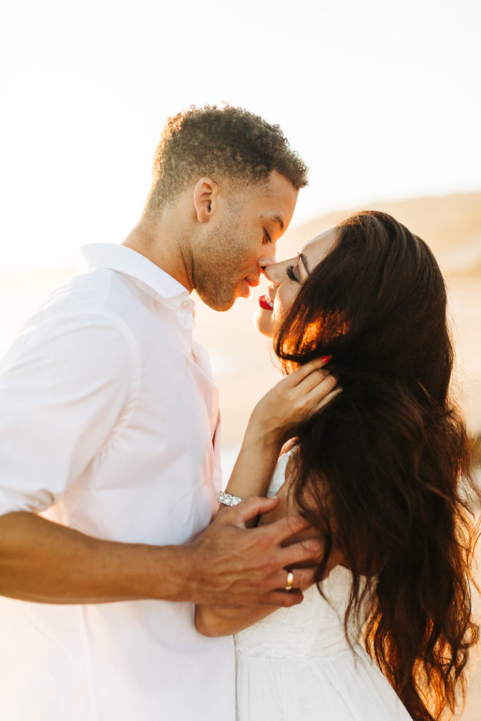 southern california engagement photos locations; couple about to kiss in romantic embrace in golden hour sunlight at crystal cove state beach