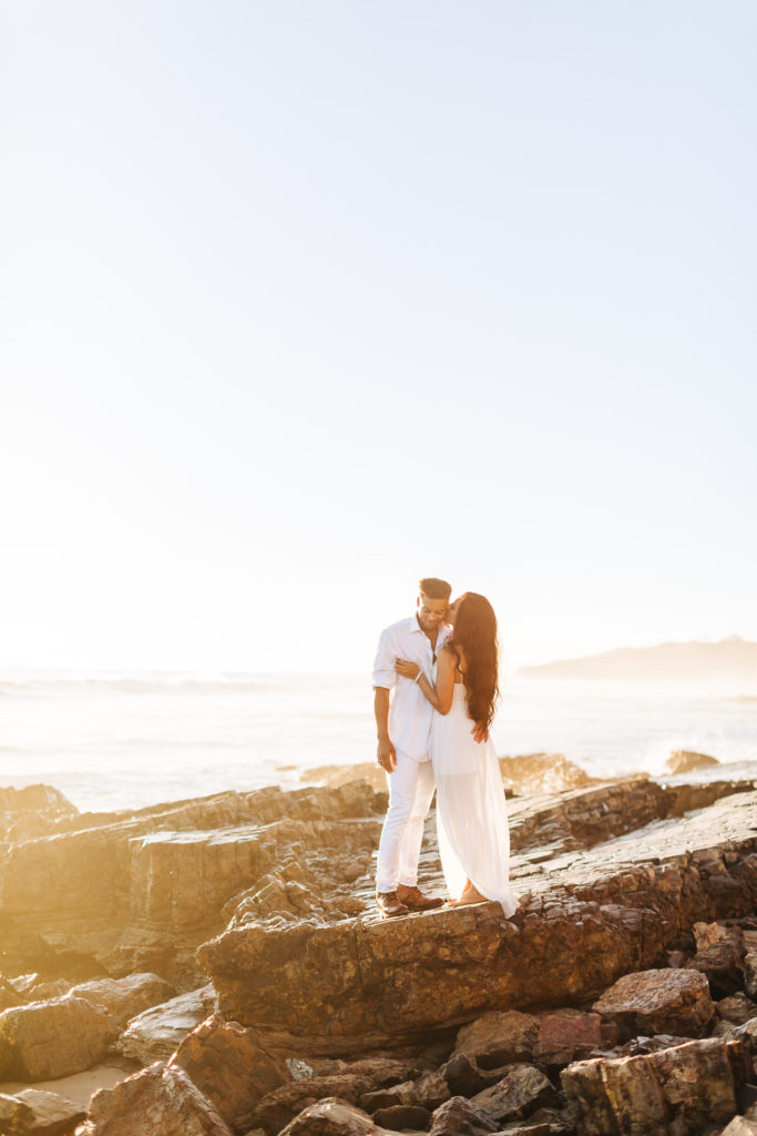 southern california engagement photos locations; couple kissing while standing on a rock at the beach