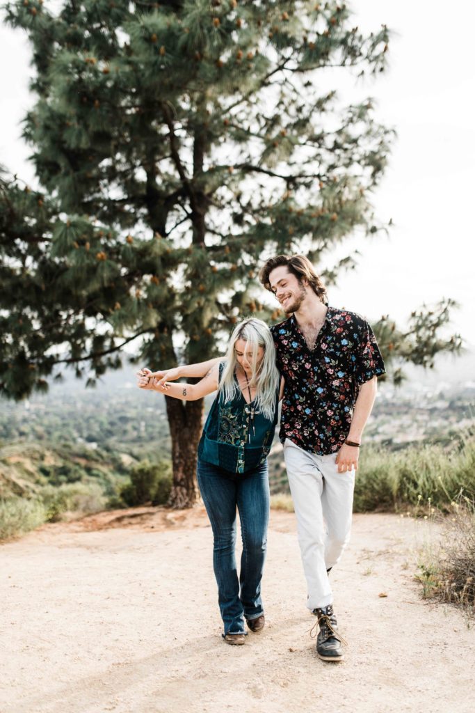 southern california engagement photos locations; couple walking holding hands on a dirt path with trees in the background