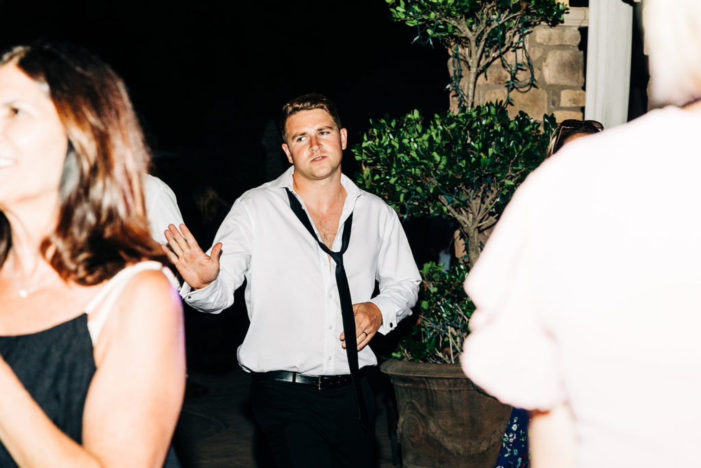Camarillo wedding photography ; groomsman unbuttons shirt while dancing at wedding reception