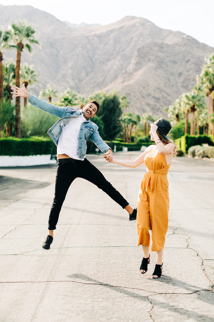 southern california engagement photos; man jumping in the air holding hands with a woman in palm springs