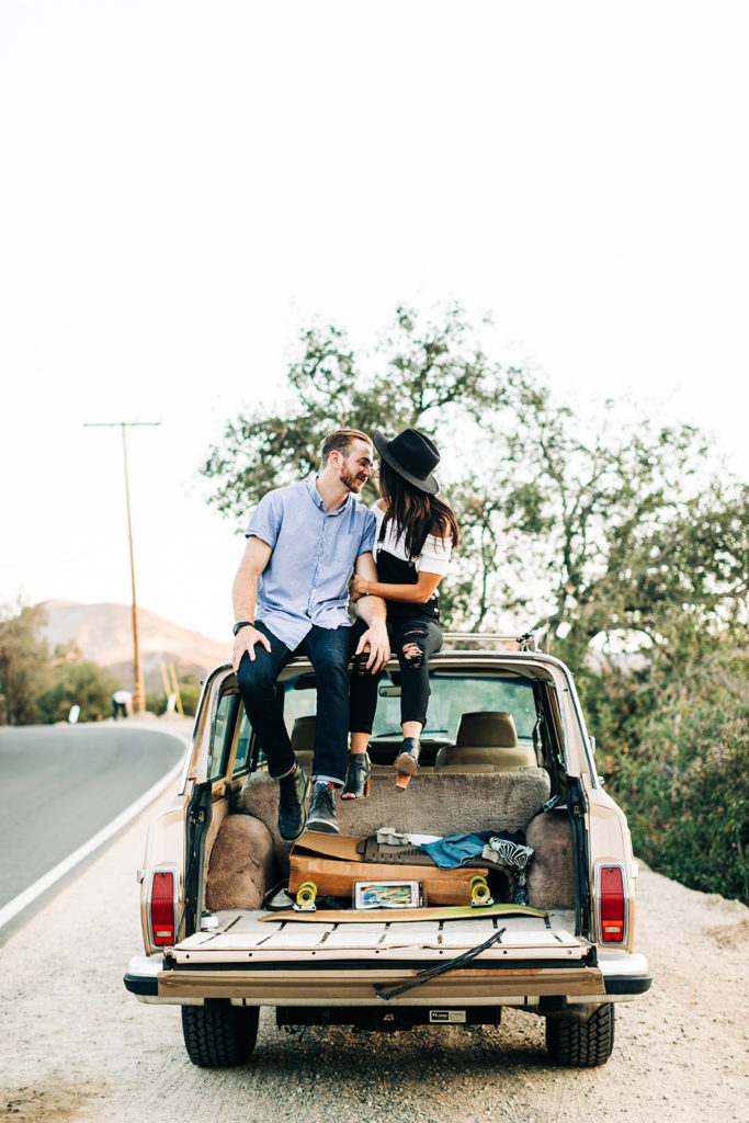 southern california engagement photos; couple sitting on top of vintage jeep grand wagoneer