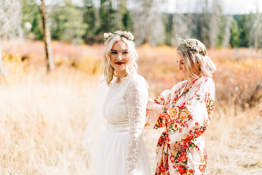 Redfish Lake Lodge wedding photography ; bridesmaid buttoning up wedding dress on bride