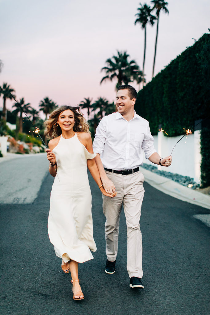 southern california engagement photos; couple running in the street holding sparklers and smiling
