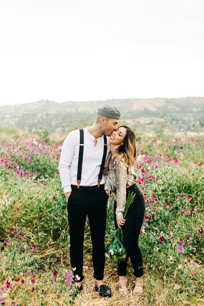 orange county engagement photos; man kissing woman on the cheek in a field of flowers
