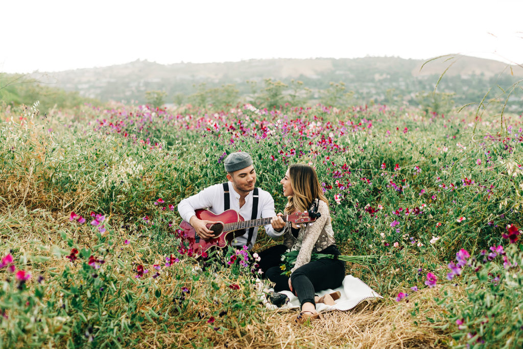orange county engagement photos; man plays guitar for woman while sitting in a field of flowers