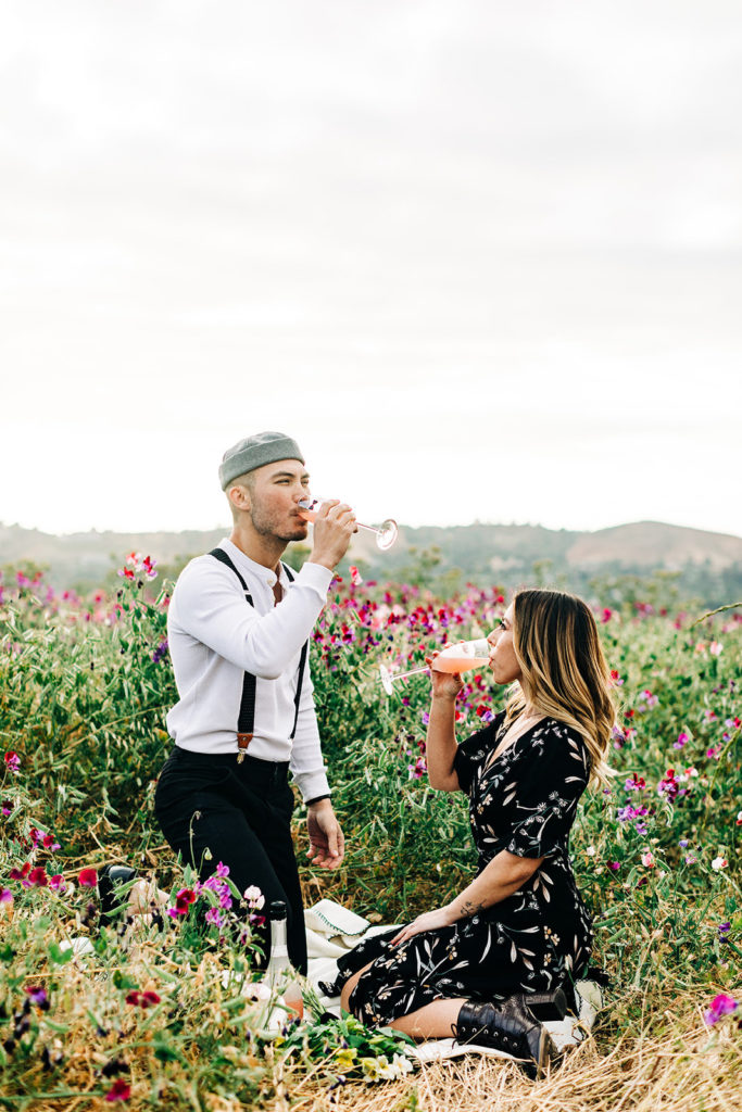 orange county engagement photos; man and woman drink champagne in a field of flowers