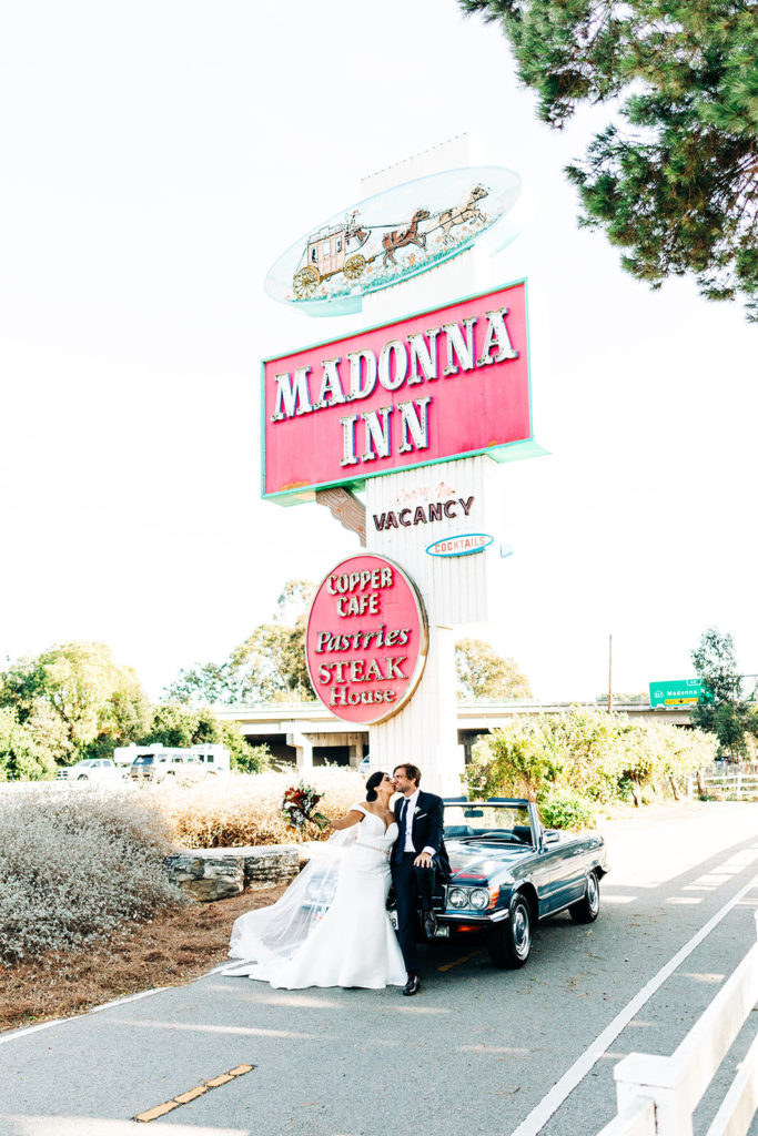 The Madonna Inn In San Luis Obispo, CA wedding photography; bride kissing his groom in front of a cafe while standing near the car