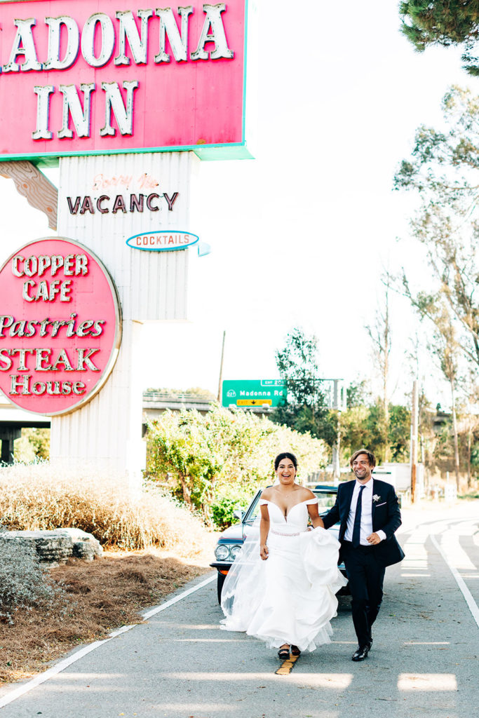 The Madonna Inn In San Luis Obispo, CA wedding photography; bride and groom walking and smiling on the road