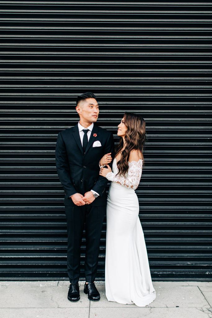 bride and groom standing against a black garage on the sidewalk outside of valentine DTLA in los angeles