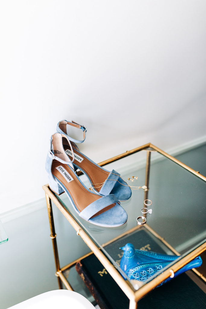 Valentine DTLA Wedding, Los Angeles wedding photographer; blue suede steve madden shoes surrounded by jewelry sitting on a glass side table