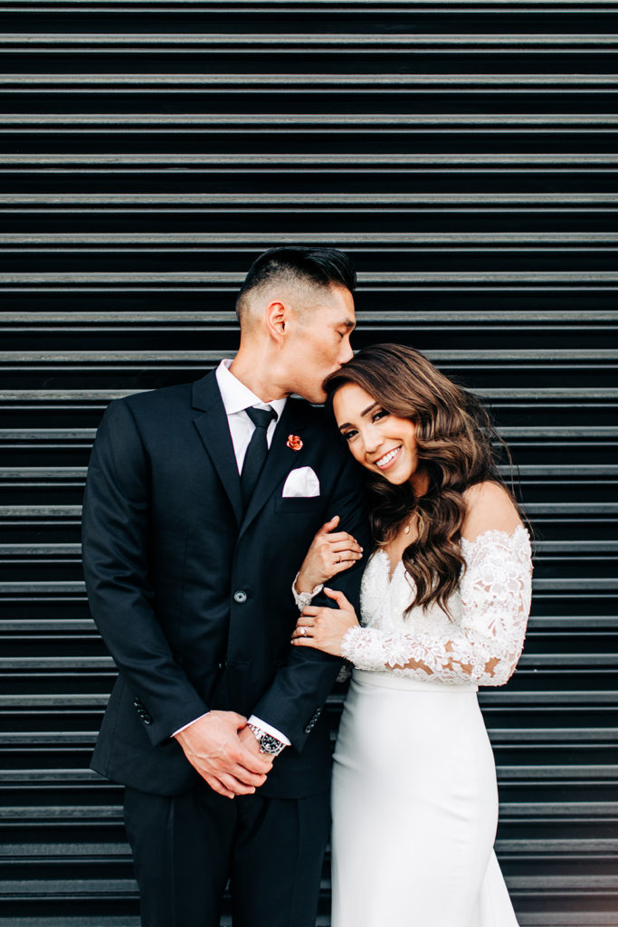 Valentine DTLA Wedding, Los Angeles wedding photographer; groom kissing the bride on her head in front of a black garage door