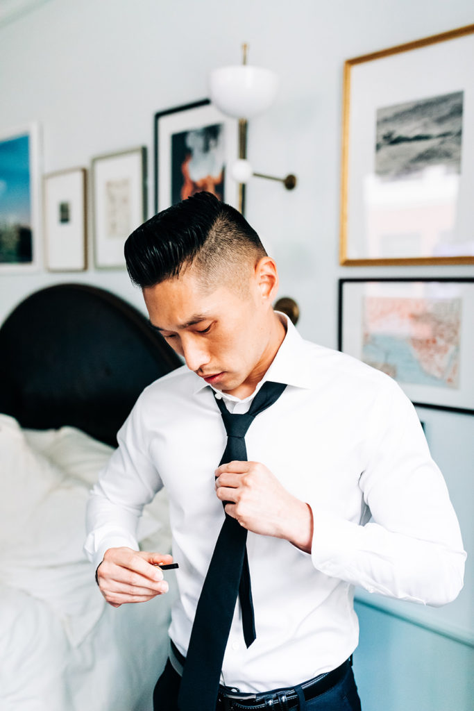 Valentine DTLA Wedding photographer; groom puts on his tie before his wedding