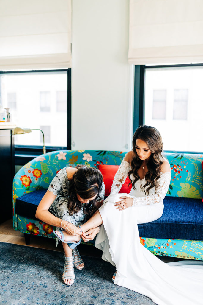 Valentine DTLA Wedding, Los Angeles wedding photographer; mother of the bride helps the bride put her shoes on while sitting on a printed couch
