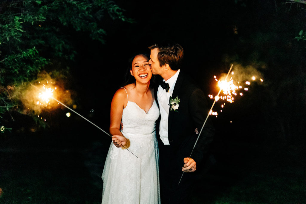 The Gold Mountain Manor In Big Bear, CA wedding photography; groom kissing her bride while holding sparkler