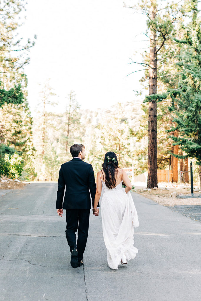 The Gold Mountain Manor In Big Bear, CA wedding photography; bride and groom walking on the uphill road in front of tall trees
