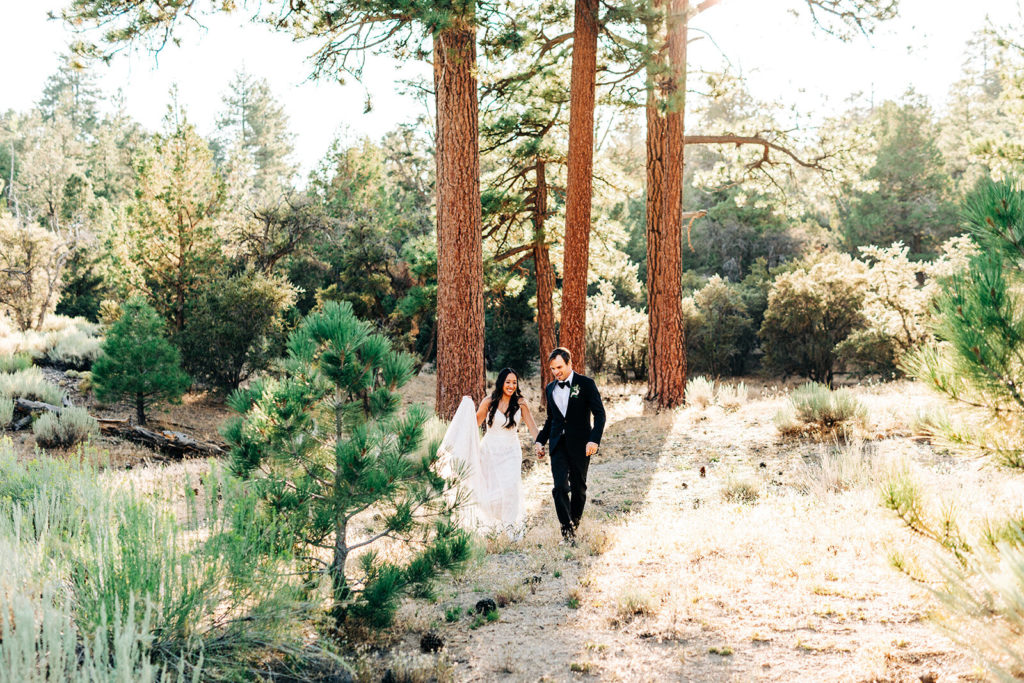 The Gold Mountain Manor In Big Bear, CA wedding photography; bride and groom walking in front of tall trees