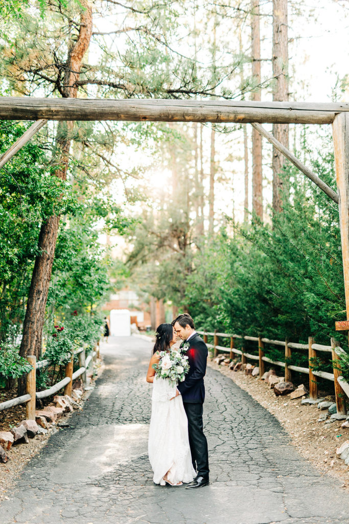 The Gold Mountain Manor In Big Bear, CA wedding photography; bride and groom about to kiss each other in front of tall green trees
