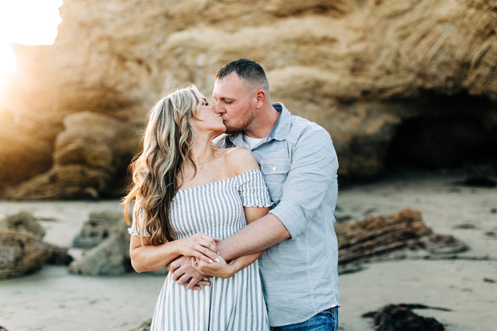 crystal cove beach engagement photos in orange county; couple kissing at the beach while man hugs woman from behind