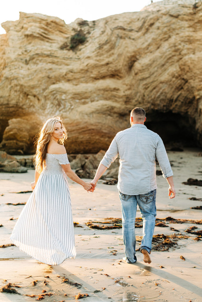 crystal cove beach engagement photos in orange county; couple walking on the beach while woman turns around and looks at the camera