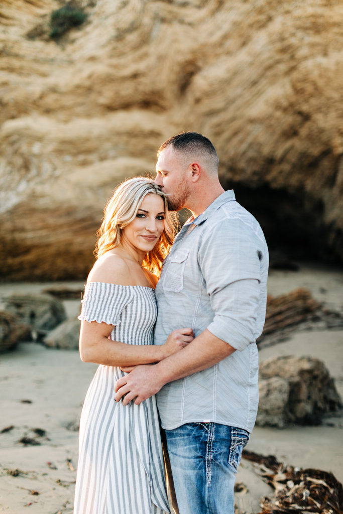 crystal cove beach engagement photos in orange county; man kisses woman on the temple while she looks at the camera on the beach