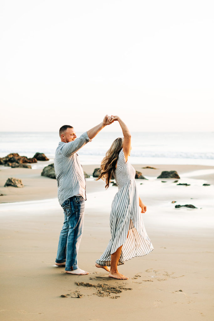 crystal cove beach engagement photos in orange county; couple dancing at the beach, man spinning woman