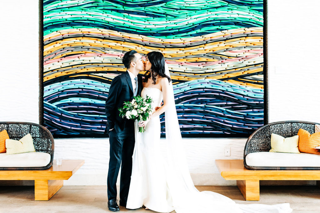 Pasea Hotel & Spa in Huntington Beach, CA wedding photography; bride and groom kissing in front of the beautiful wall painting