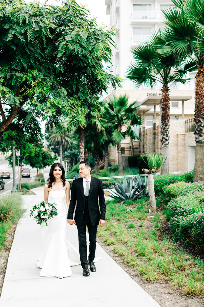 Pasea Hotel & Spa in Huntington Beach, CA wedding photography; bride and groom walking together on the path with the greenish background