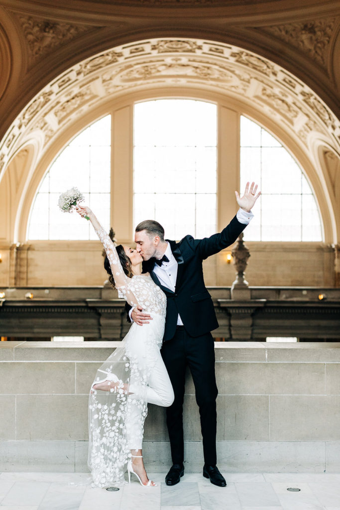 City Hall in San Francisco, CA wedding photography; bride and groom kissing with hands in the air