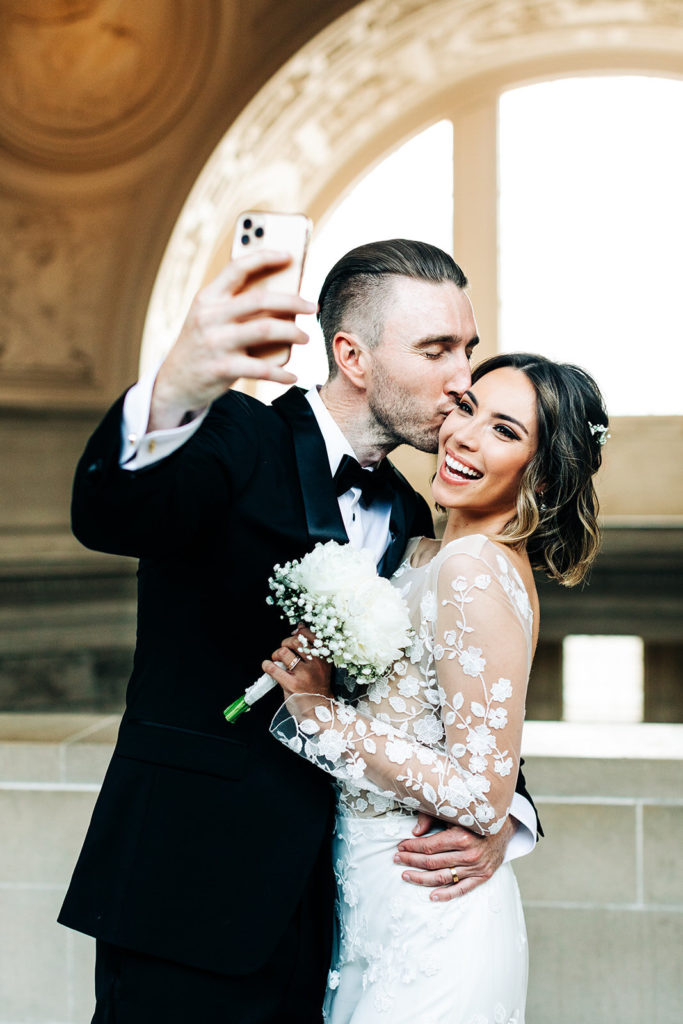 City Hall in San Francisco, CA wedding photography; groom kissing his bride and taking selfie