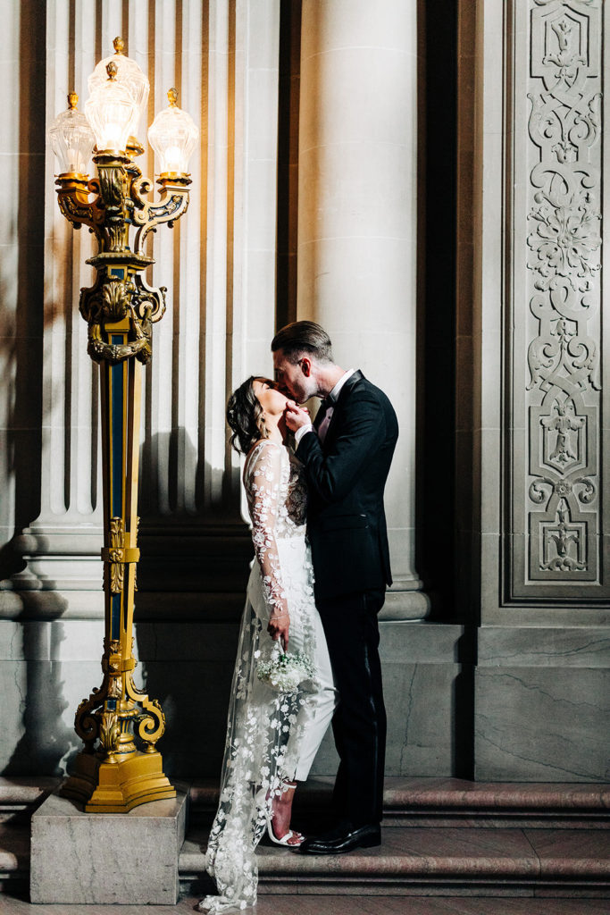 City Hall in San Francisco, CA wedding photography; bride and groom kissing while standing near the lighting pole