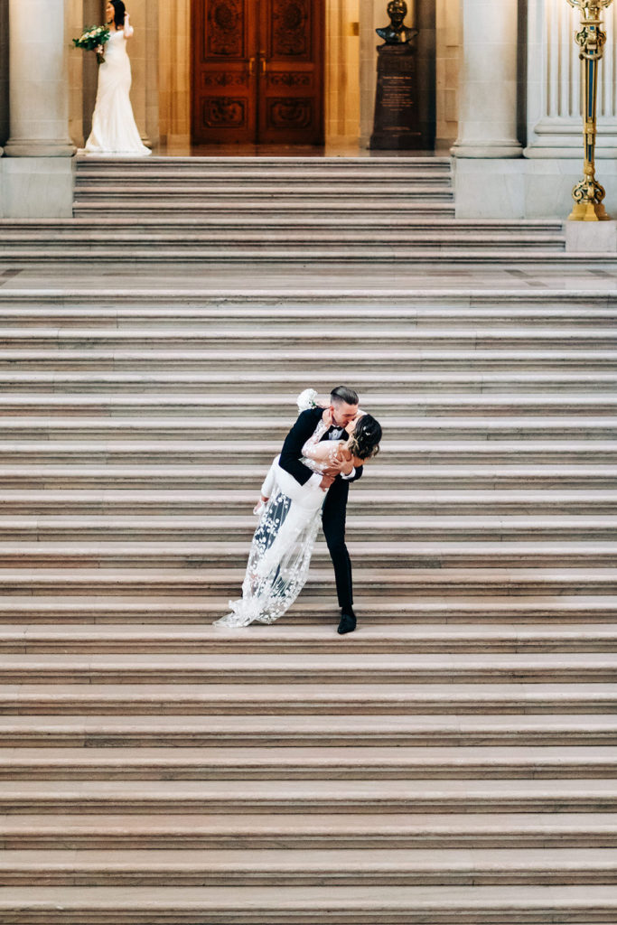 City Hall in San Francisco, CA wedding photography; bride and groom kissing between the stairs