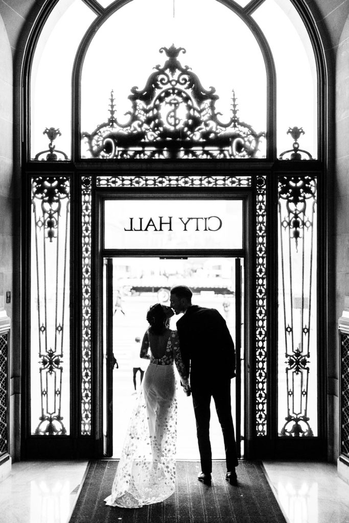 City Hall in San Francisco, CA wedding photography; bride and groom kissing at the exit door of City Hall