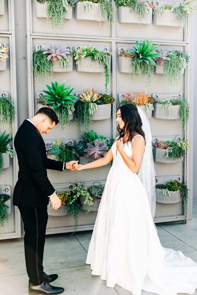 Colony house in Anaheim, CA wedding photography; groom holding bride's hand in front of beautiful wall having plants