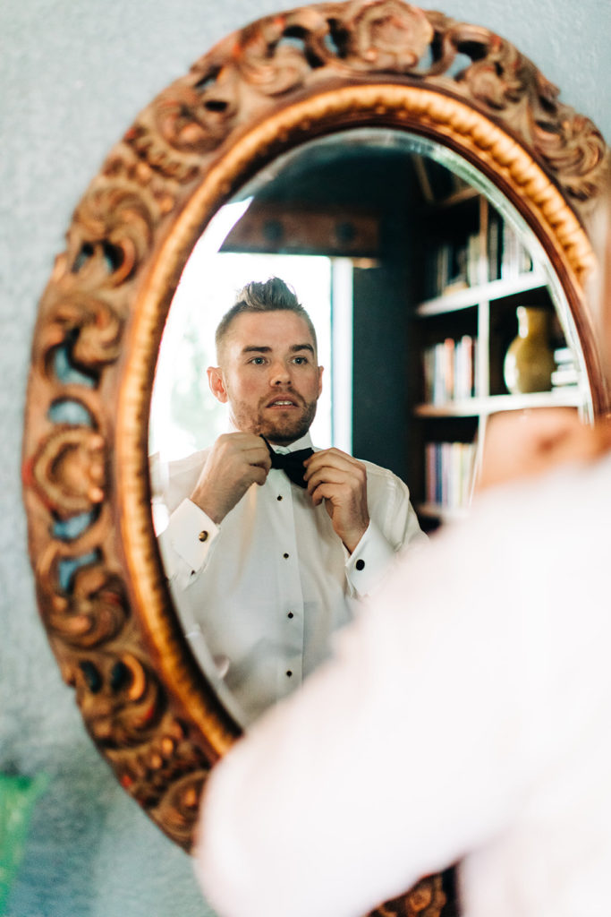 Avalon Legacy Ranch wedding photography; groom adjusting his neck bow while watching into the mirror