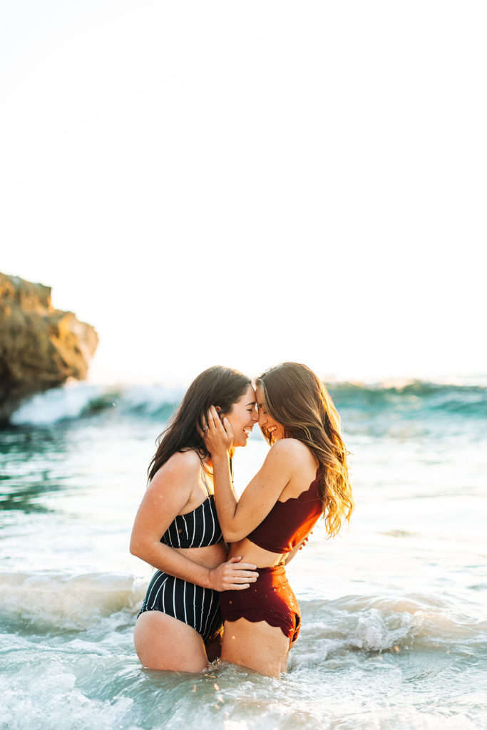 laguna beach engagement photos; lesbian couple smiling in the waves on the beach in laguna beach, ca