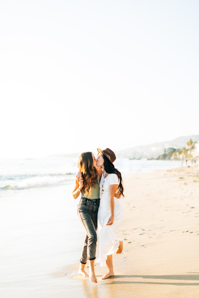 lesbian couple walking and kissing on the beach in laguna beach, ca