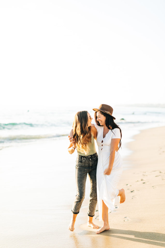 lesbian couple walking and smiling on the beach in laguna beach, ca