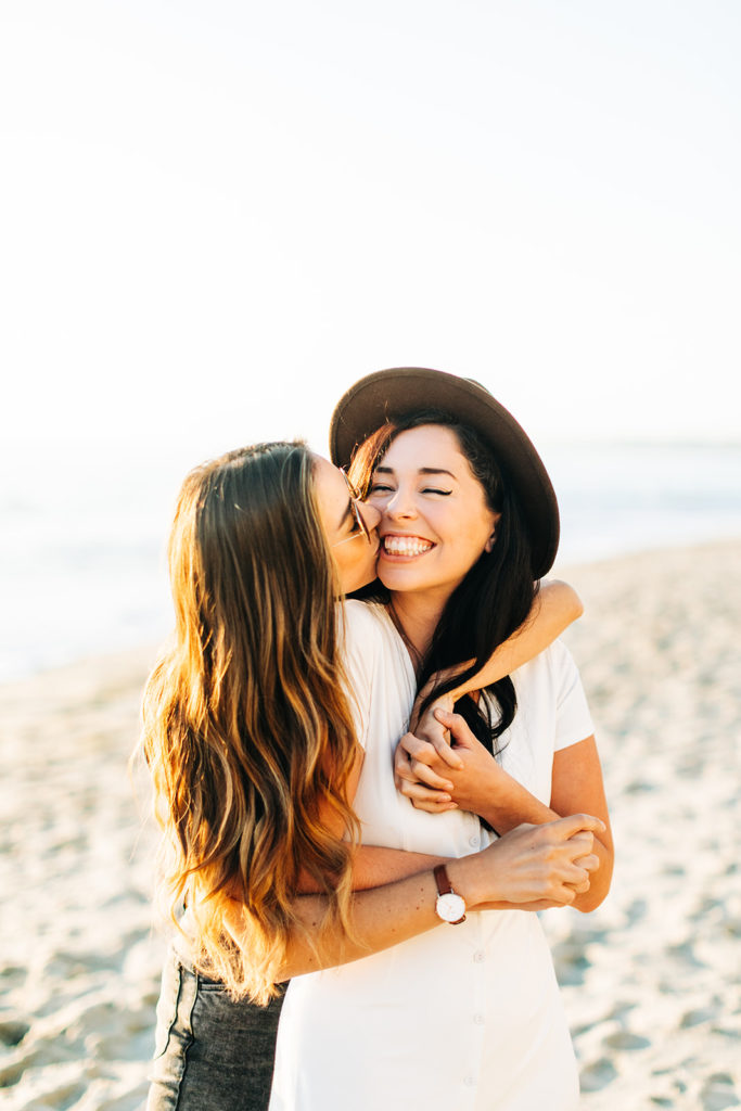 laguna beach engagement photos; lesbian couple smiling and kissing on the cheek on the beach in laguna beach, ca
