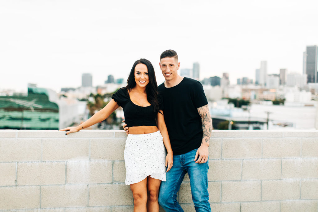 rooftop engagement photos in los angeles; a couple smiling on a rooftop with buildings in the background in los angeles, ca