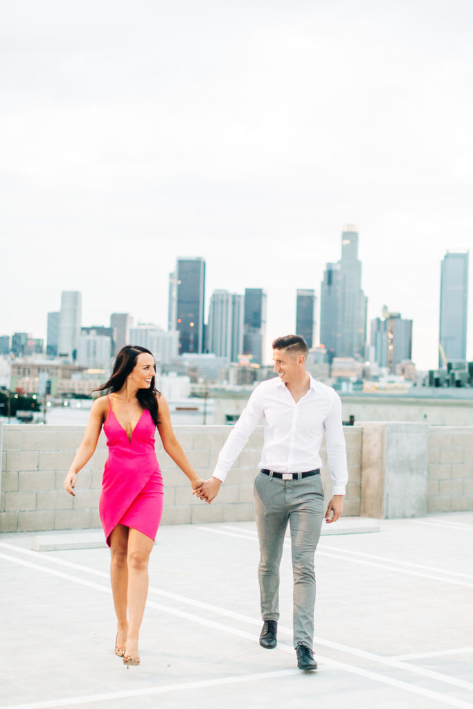 rooftop engagement photos in los angeles; a couple in formal outfits walking on a rooftop with buildings in the background in los angeles, ca