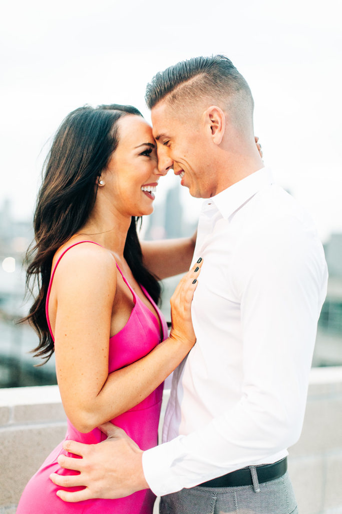 rooftop engagement photos in los angeles; a couple in formal outfits hugging on a rooftop with buildings in the background in los angeles, ca