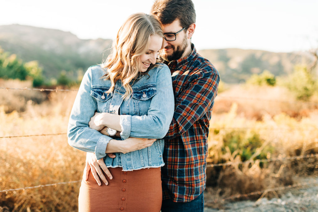 southern california engagement photos; couple hugging with hills in the background in santiago canyon