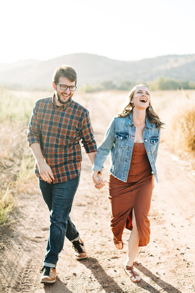 southern california engagement photos; couple walking down a dirt path and laughing