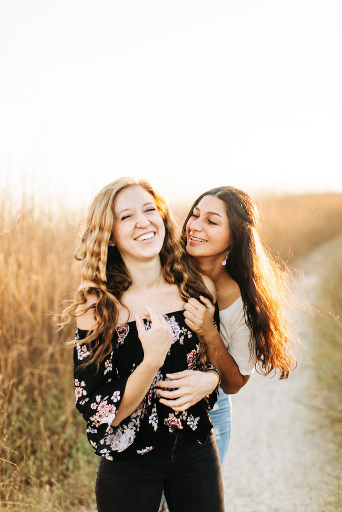 LGBTQ+ wedding photographer; a woman laughing while her girlfriend hugs her from behind