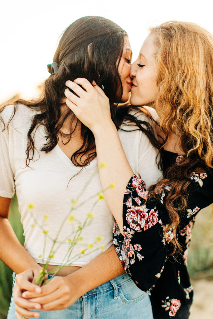 LGBTQ+ wedding photographer; two women embracing each other lovingly and kissing while holding wildflowers