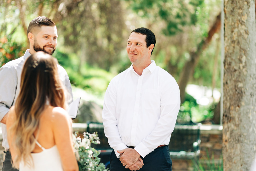 groom smiling at the officiant on his wedding day with his bride blurred in the foreground; orange county elopement photographer