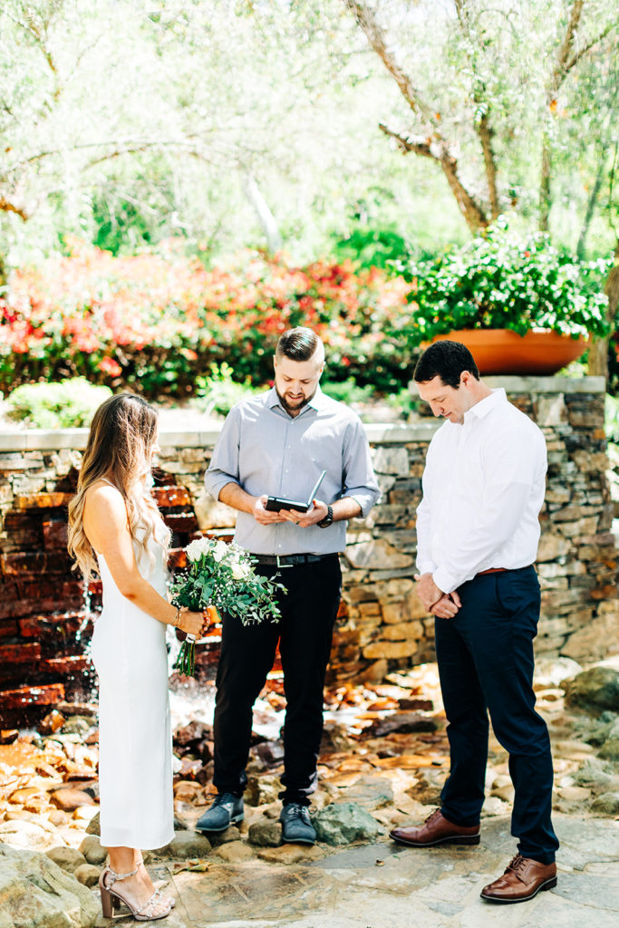 bride and groom and officiant bow their heads in prayer at an outdoor wedding; orange county elopement photographer
