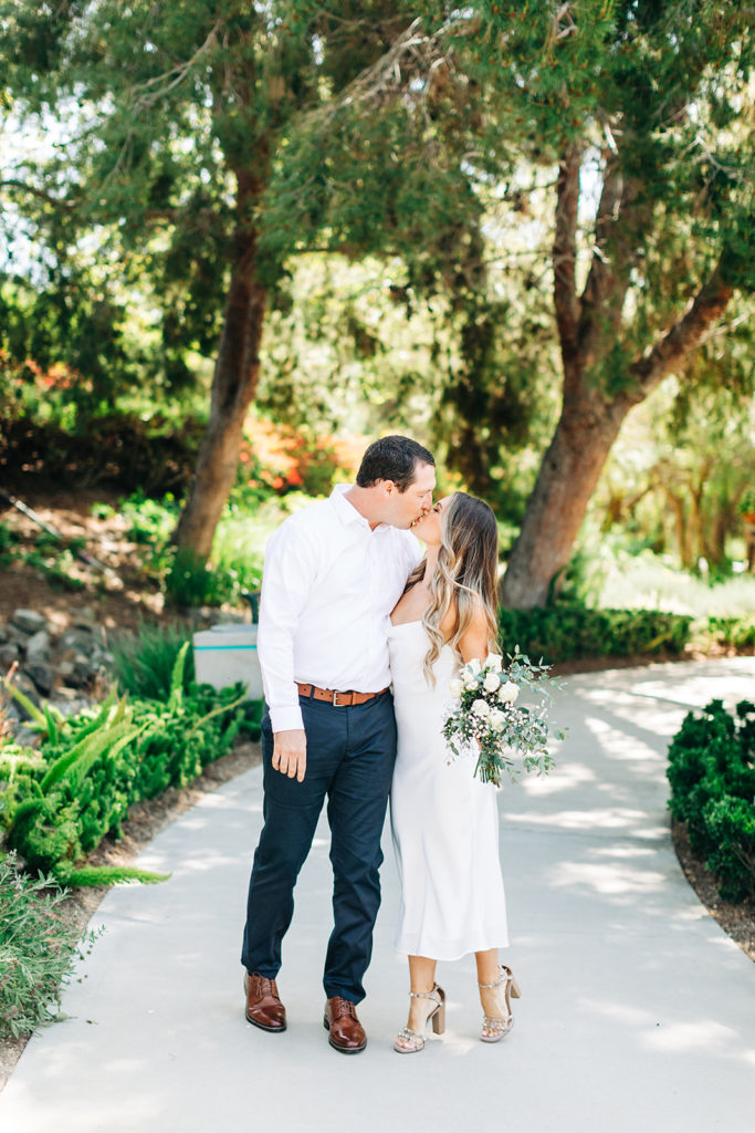 bride and groom holding flowers and kissing at an outdoor wedding; orange county elopement photographer