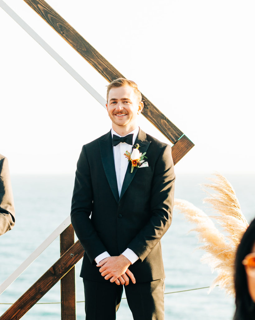 Crystal Cove Micro Wedding in Orange County; groom smiling as he sees his bride walking down the aisle
